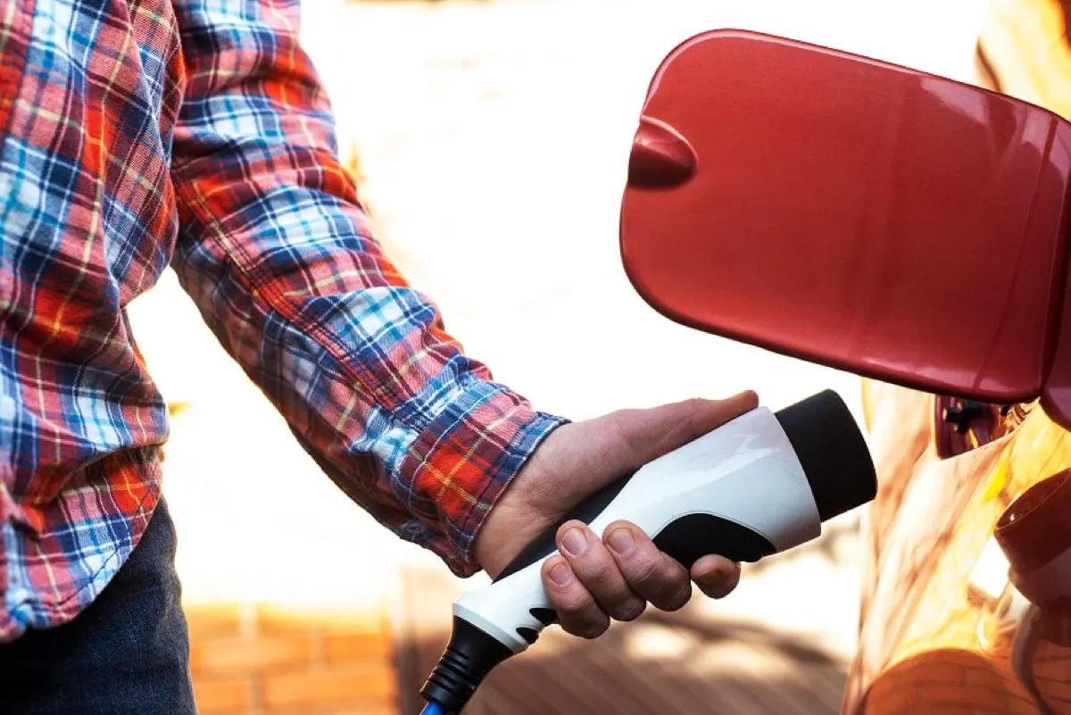 Male model stands by an electric car and holds a charging plug