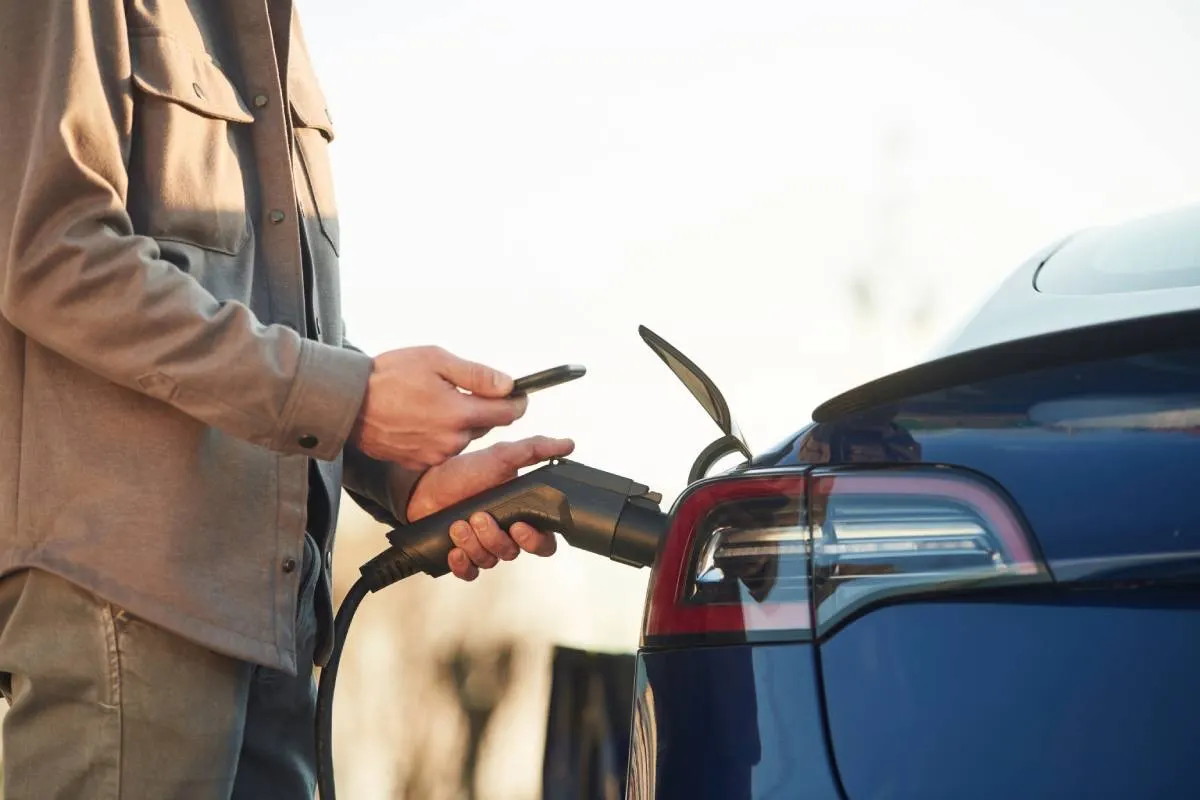 close up shot of a man looking at his phone while charging an electric car