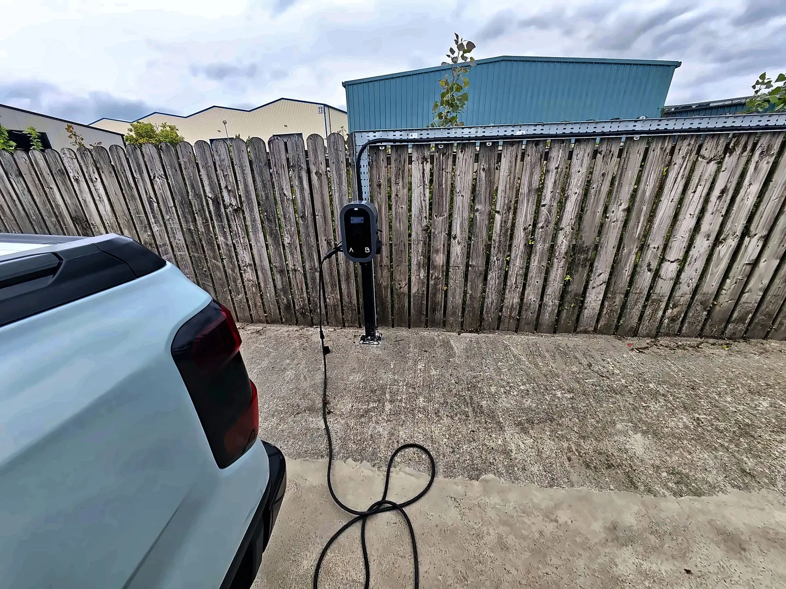 Home EV charger installed by Glow on a fence post beside the car