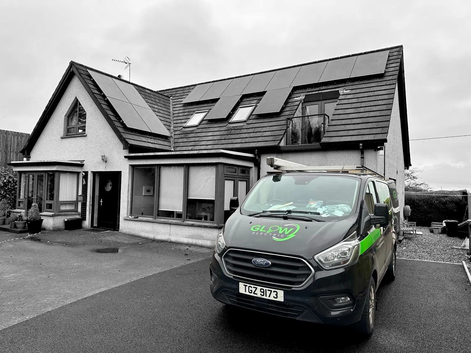 Glow van in full colour against a monochrome street — a finished all-black solar installation behind it