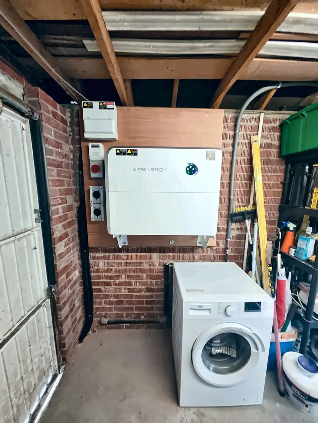 Wall-mounted Sigenergy SigenStor in a domestic garage, clear of the floor beside the washing machine — Glow install, east Belfast